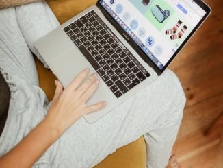 Une femme utilise un ordinateur portable pour parcourir ses achats en ligne, assise confortablement dans un cadre intérieur chaleureux.