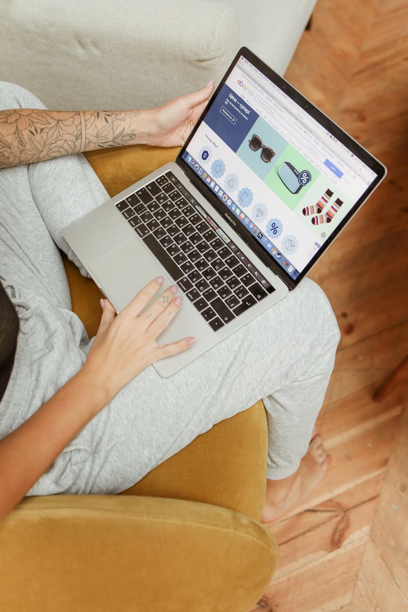 Une femme utilise un ordinateur portable pour parcourir ses achats en ligne, assise confortablement dans un cadre intérieur chaleureux.